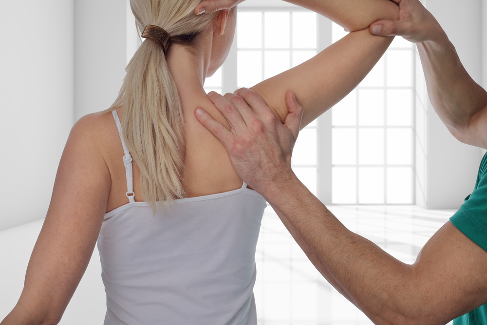 A physical therapist guides a woman through a shoulder mobility exercise in a well-lit room - manual adjustment A physical therapist guides a woman through a shoulder mobility exercise in a well-lit room - manual adjustment