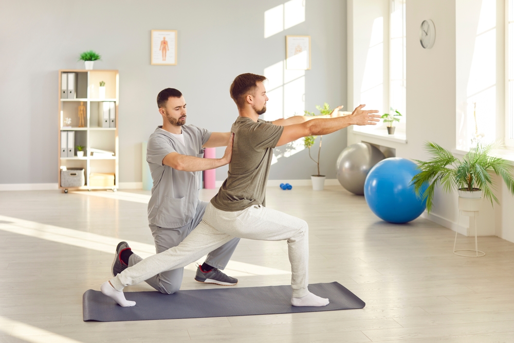 A chiropractor helps guide a patient through a stretching exercise in a bright therapy room - Chiropractor Irving TX A chiropractor helps guide a patient through a stretching exercise in a bright therapy room - Chiropractor Irving TX