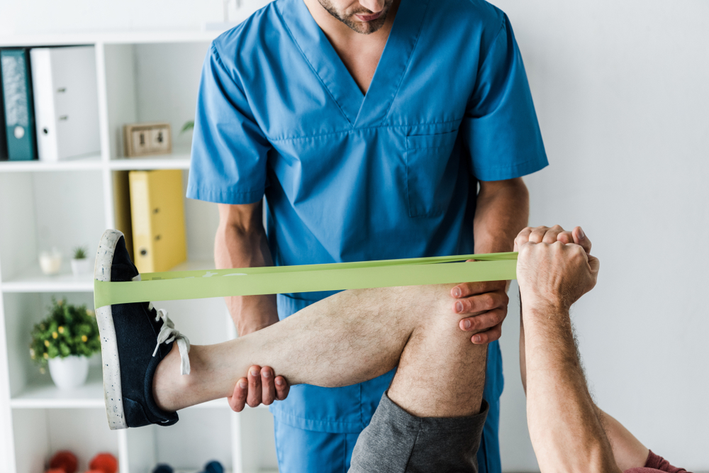 A chiropractor assists a patient with resistance band exercises for leg rehabilitation - Chiropractor Irving TX A chiropractor assists a patient with resistance band exercises for leg rehabilitation - Chiropractor Irving TX
